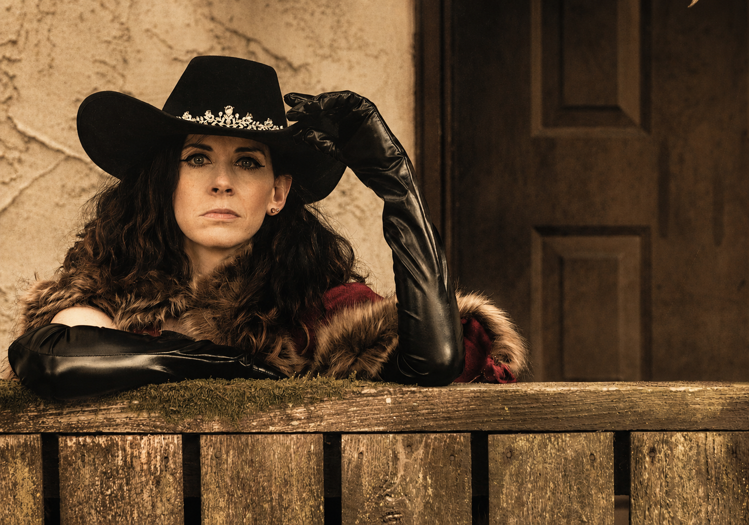 Melissa Endean leaning on a wooden fence in cowboy hat and leather gloves