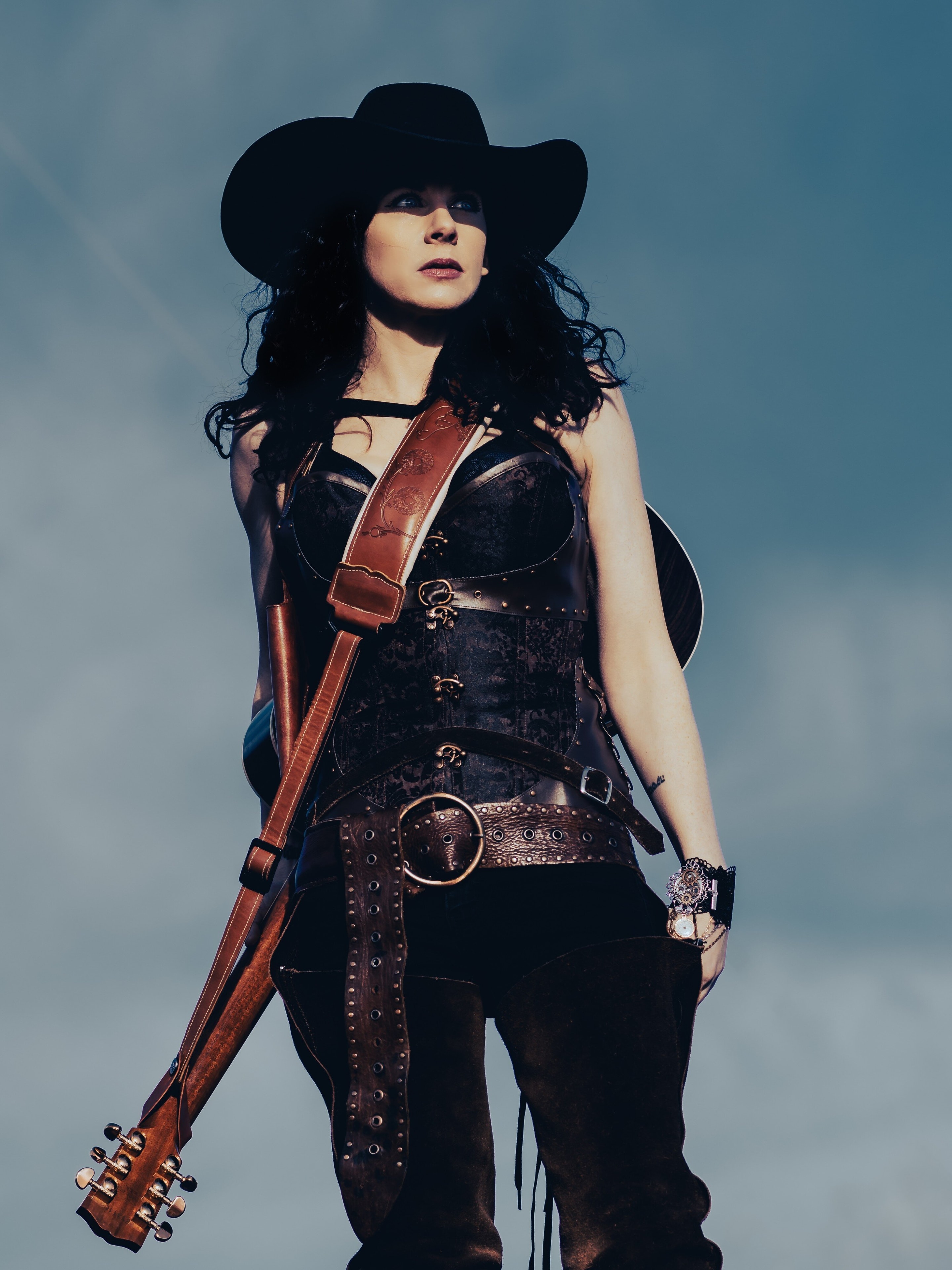 Melissa Endean standing in a field with her Gibson guitar in cowboy hat and leather outfit