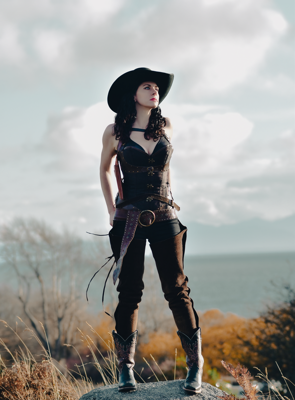Melissa Endean standing on a hilltop in cowboy hat and leather outfit with ocean in the background